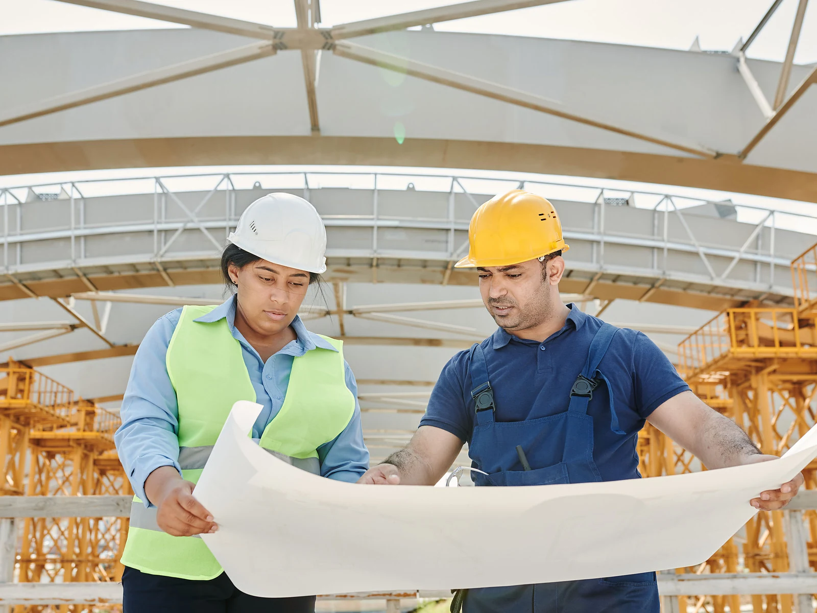 Two engineers in hard hats reviewing construction plans together on site